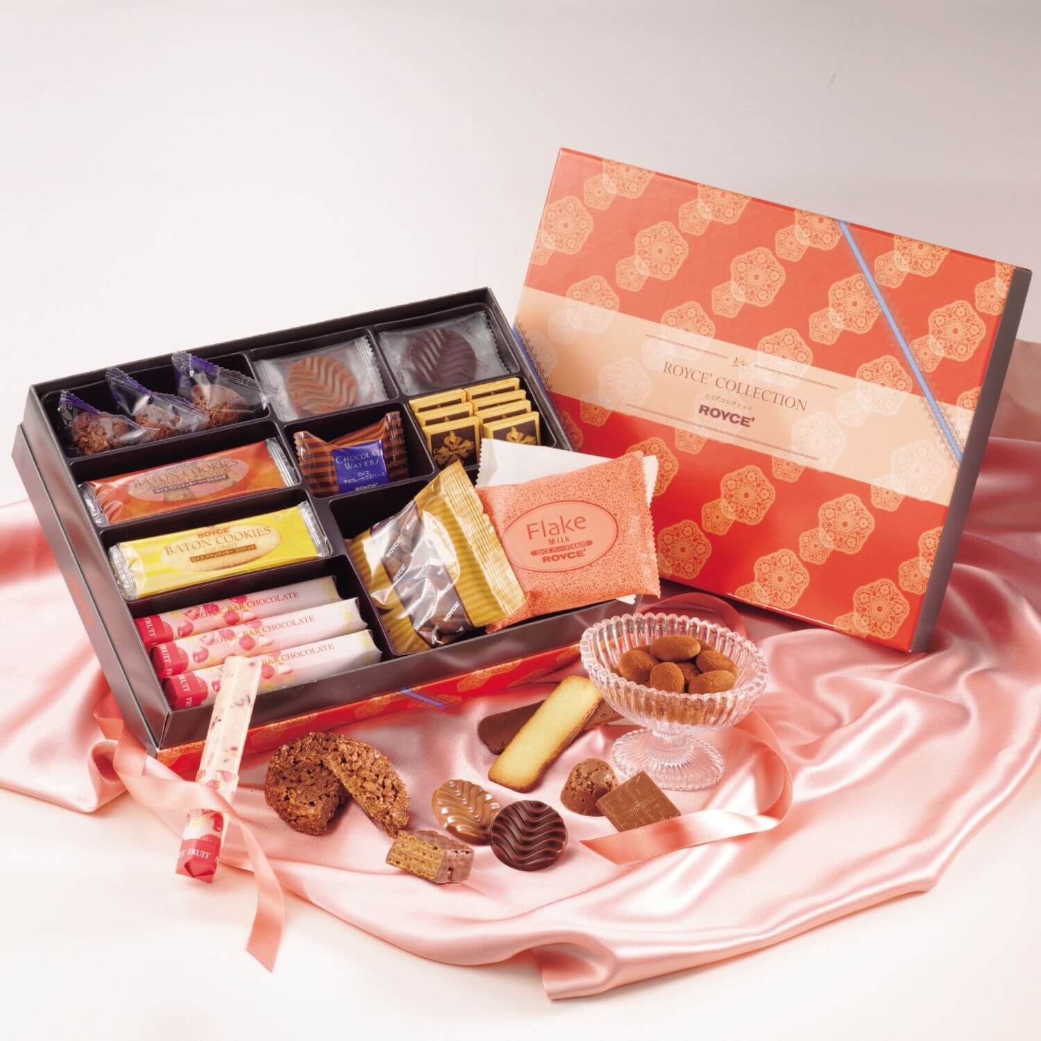 ROYCE' Chocolate - Image shows chocolate boxes with confections inside and accents of loose chocolates and a pink silk tablecloth.