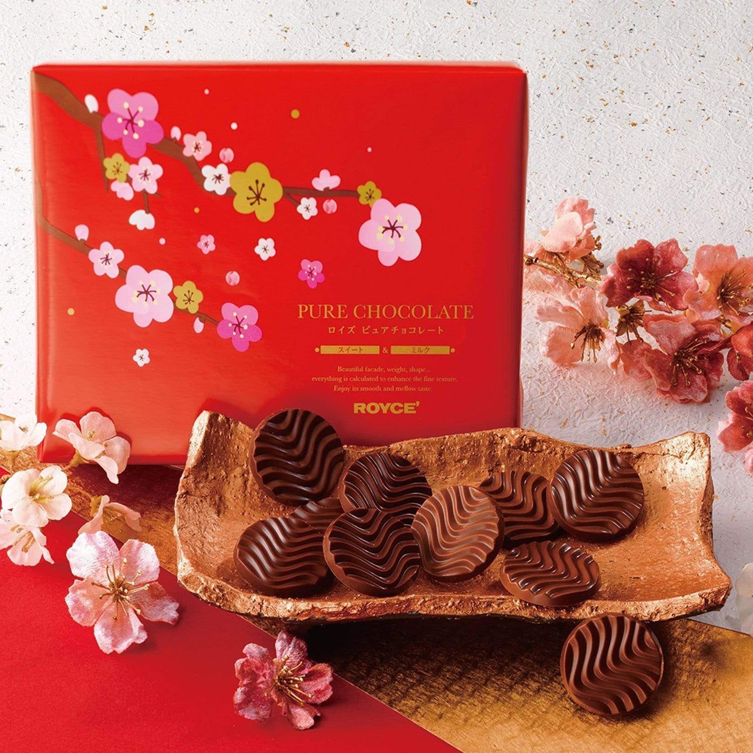 Image shows chocolate discs on a plate with flowers and a red box.