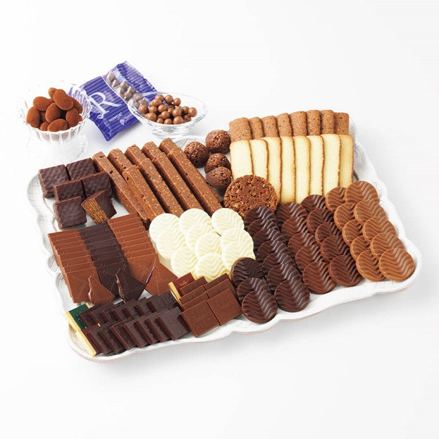 ROYCE' Chocolate - ROYCE' Collection "Brown" - ROYCE' Collection "Brown" with Prafeuille Chocolat "Orange" - Image shows various chocolates and confections in different shapes and colors, as arranged on a white tray with clear bowls and a blue-violet pack on top left. Background is in white.