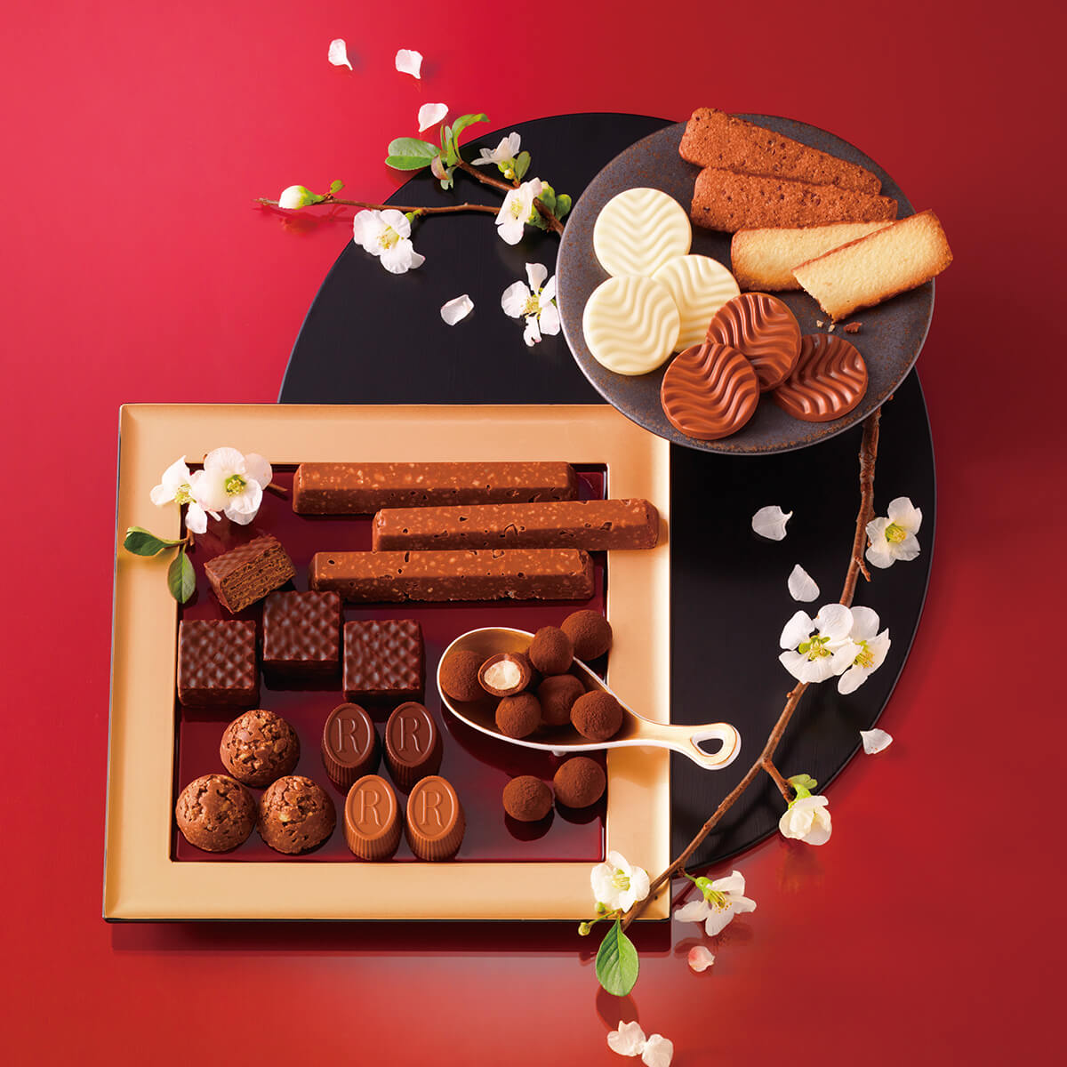 ROYCE' Chocolate - Image shows different kinds of chocolates in square- and circle-shaped plates. Accents include flowers and a serving spoon. Background is in red. 