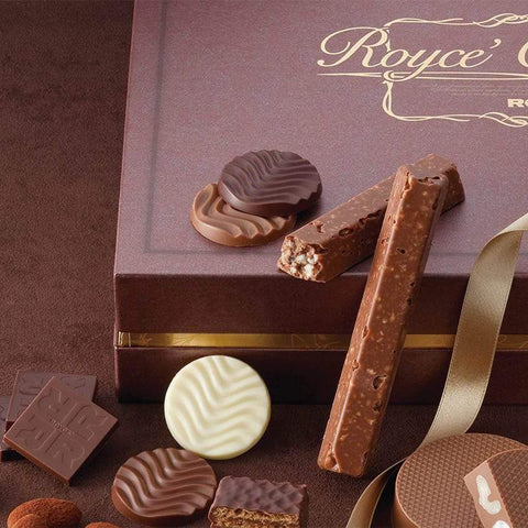 ROYCE' Chocolate - ROYCE' Collection "Brown" - Image shows a brown box. Gold text says ROYCE' Collection ROYCE'. Below are confections and chocolates in different shapes and colors. Accent includes a gold silk ribbon. Background is in the color brown.